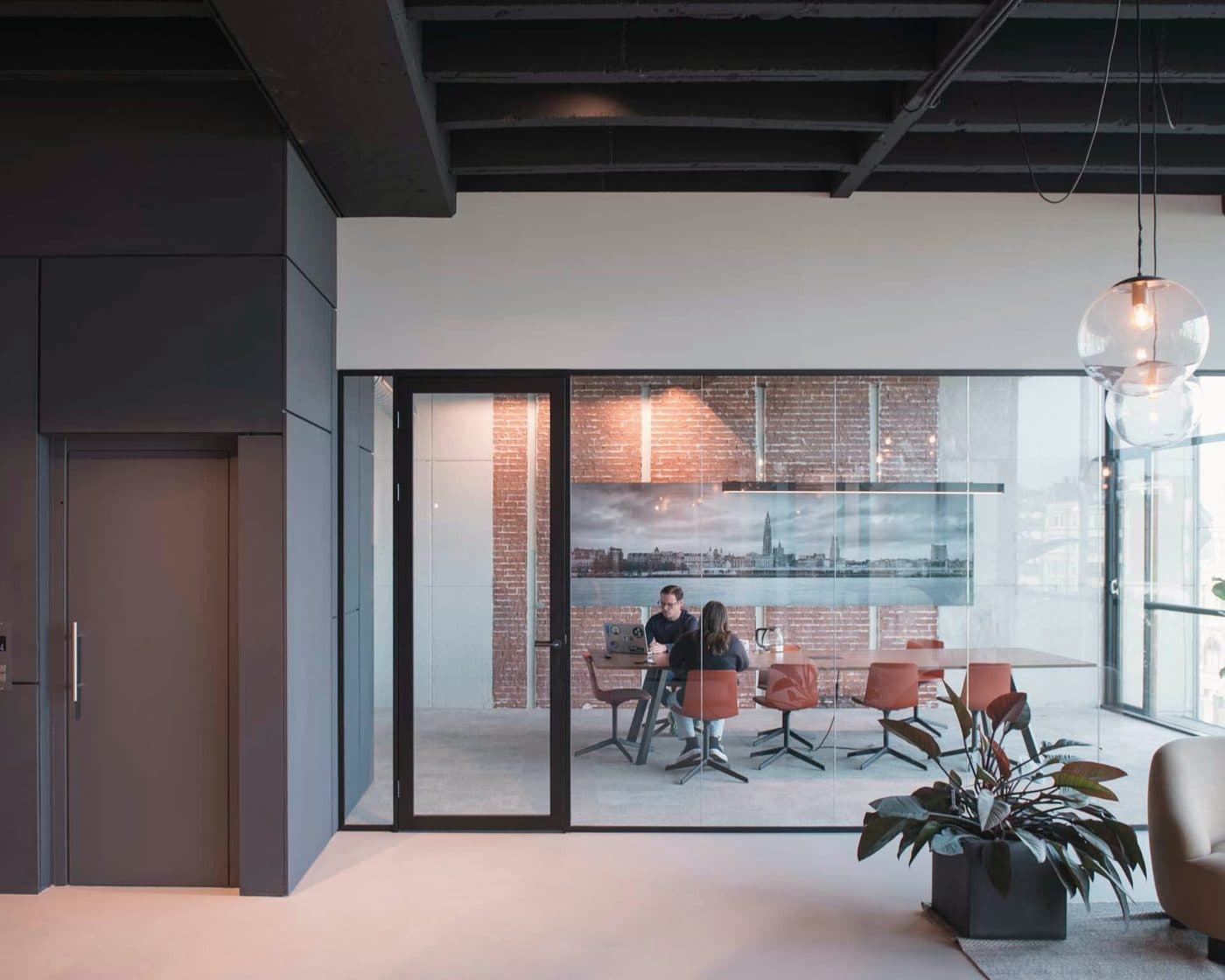 Twee collega's in de vergaderzaal, met de skyline van Antwerpen aan de muur